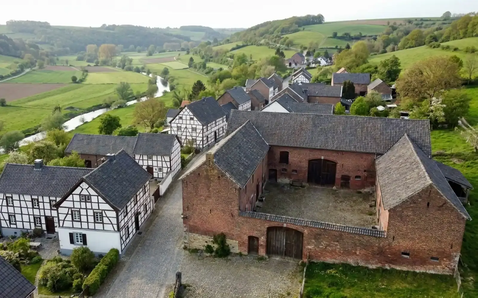 Heuvelachtig landschap met vakwerkhuizen en een bakstenen hoeve